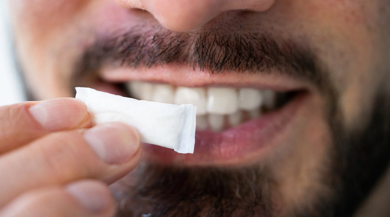 Nahaufnahme einer Hand, die einen weißen Nicotine Pouch vor dem Mund hält. 