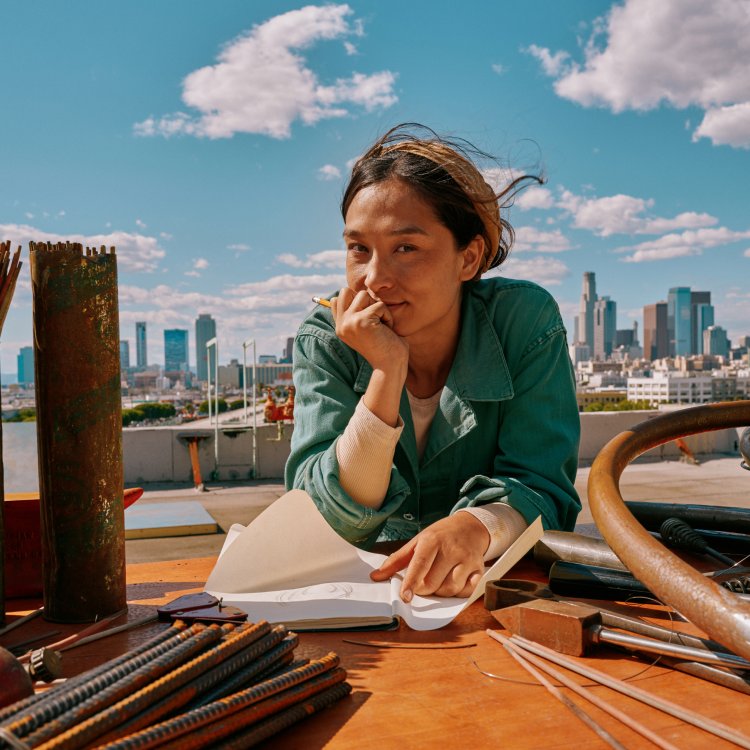Variante recortada de mujer dibujando con un IQOS Iluma i ONE azul frente al skyline.