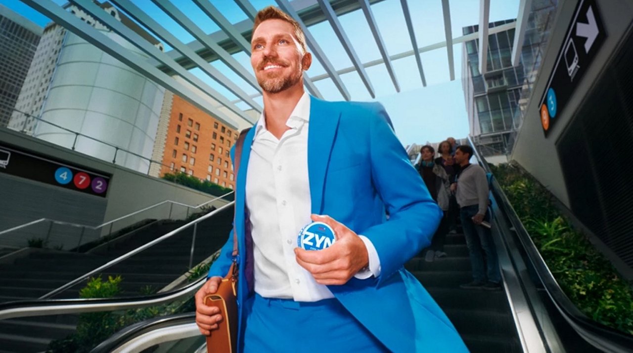 Person in blauem Anzug hält eine ZYN-Dose in der Hand und geht eine Rolltreppe hinunter.