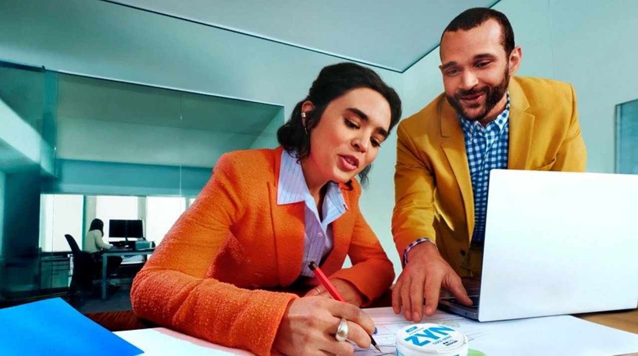 Zwei Personen arbeiten gemeinsam an einem Schreibtisch, ZYN-Dose liegt gut sichtbar auf den Unterlagen vor ihnen.