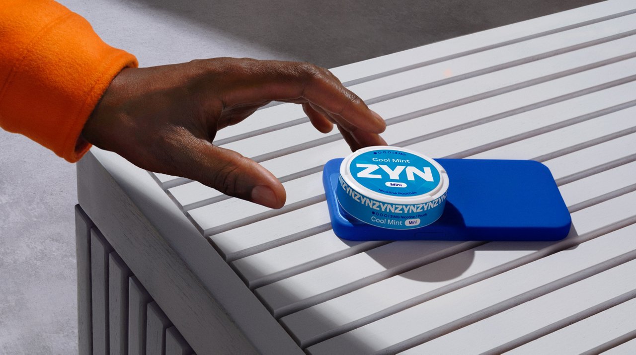 Nahaufnahme einer Hand, die einen weißen Nicotine Pouch vor dem Mund hält. 