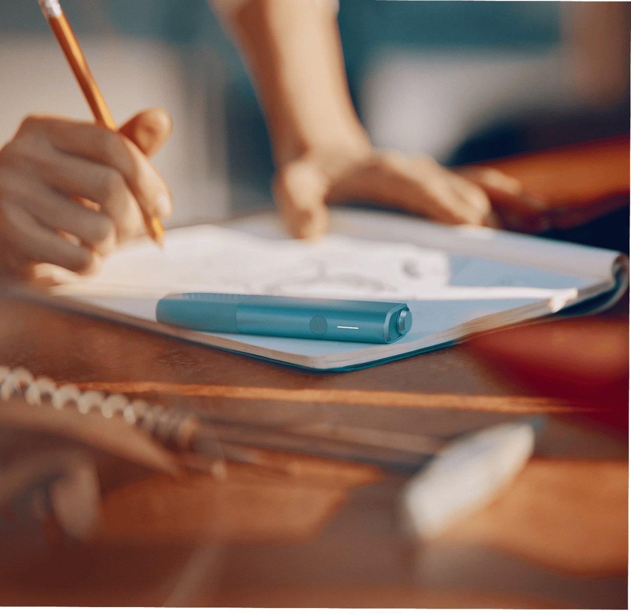 A person holding a pencil on their hand with an IQOS ILUMA i ONE color Breeze Blue on top of the notebook