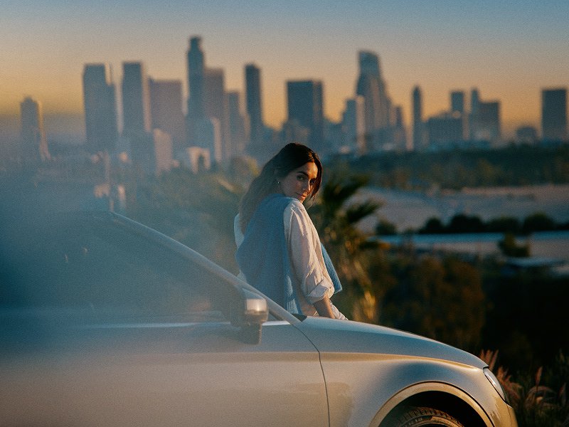 Mujer sentada sobre un carro viendo el atardecer en una ciudad
