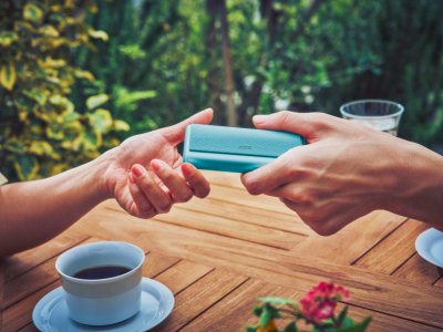 Two people exchanging a turquoise IQOS package across an outdoor table with coffee cups.
