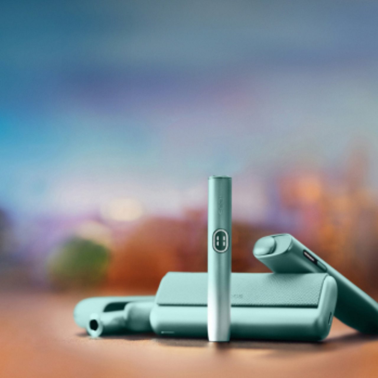 The IQOS ILUMA i range of devices in Breeze Blue against a soft pastel background with blurred shades of blue, purple, and green creating a calm, modern aesthetic.