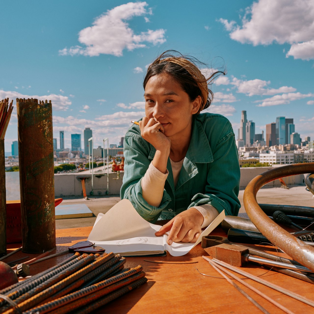 Mujer dibujando al aire libre con un IQOS Iluma i ONE azul sobre la mesa y skyline al fondo.
