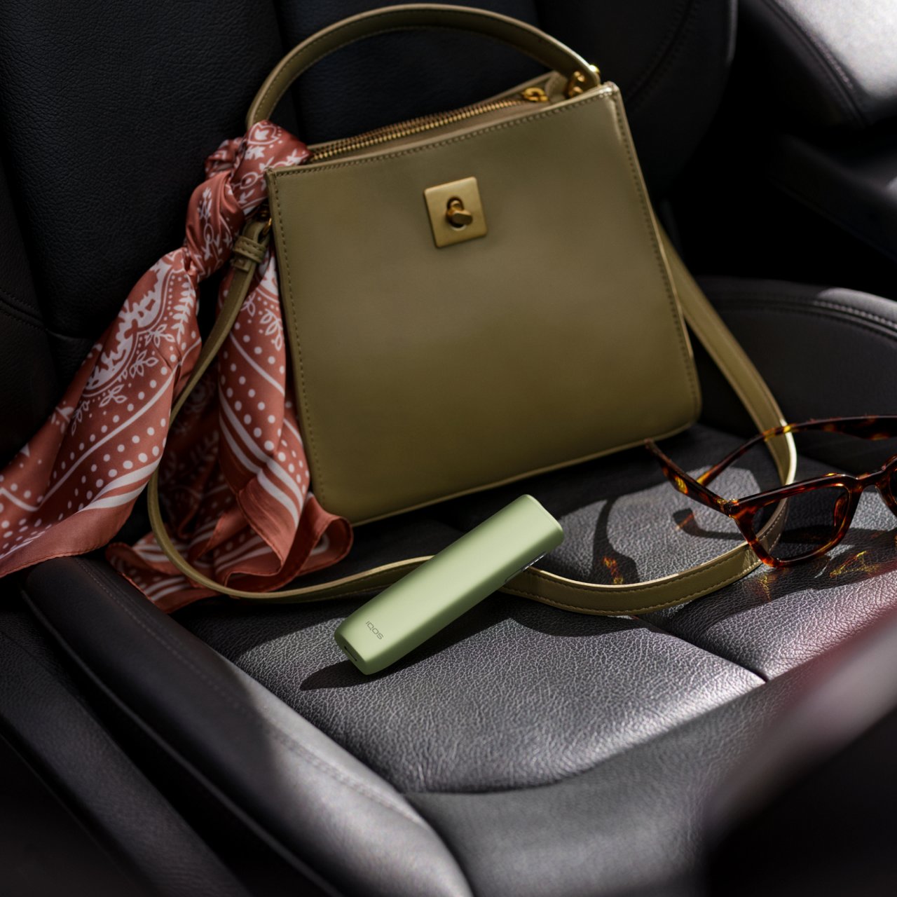 IQOS ILUMA i One color turquesa dentro de una bolsa verde en el asiento del auto.