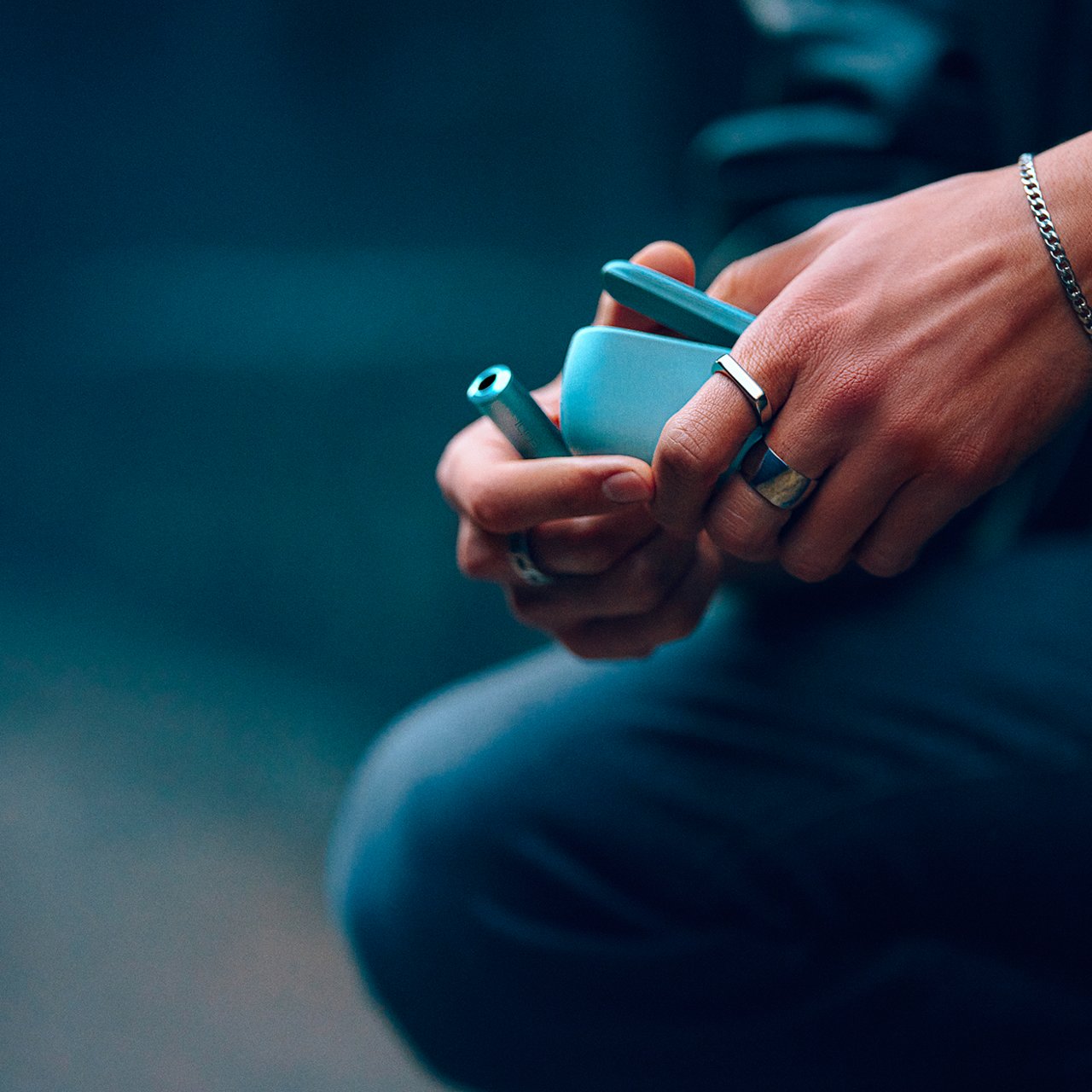 Persona usando IQOS Iluma i verde mientras abre el cargador en ambiente interior