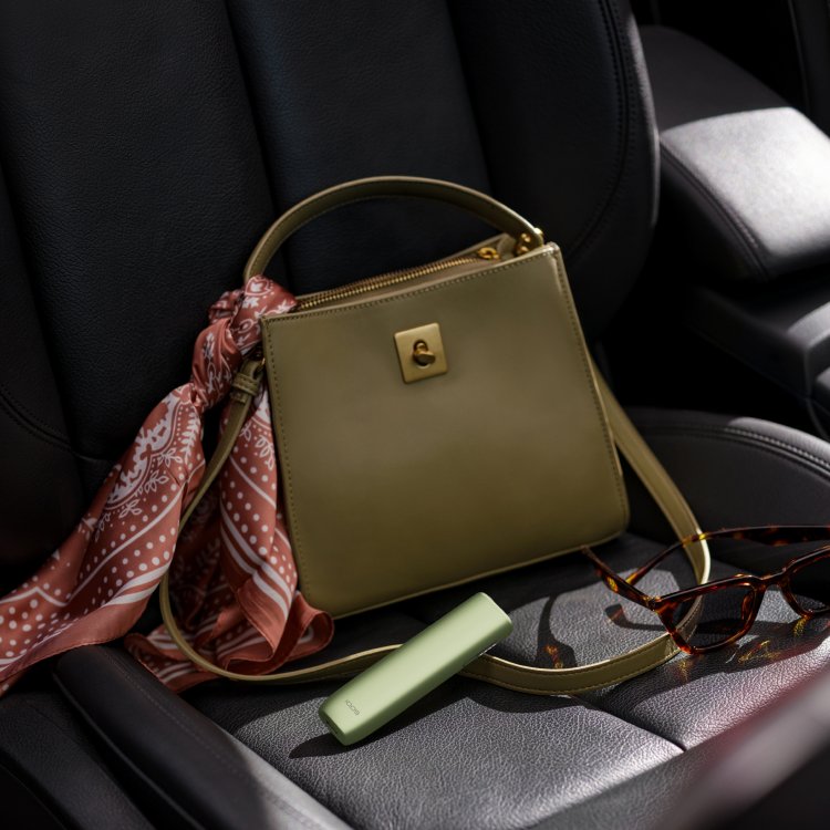 IQOS ILUMA i One color turquesa dentro de una bolsa verde en el asiento del auto.