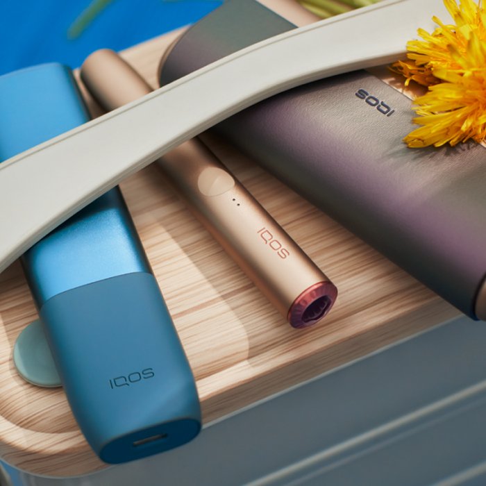  Zařízení IQOS ILUMA a příslušenství ležící na stole s květinou