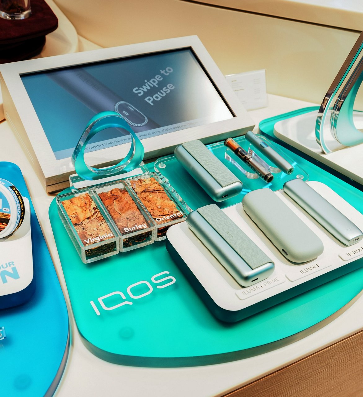 Retail display of IQOS ILUMA i devices with tobacco samples and digital screen and turquoise IQOS key.