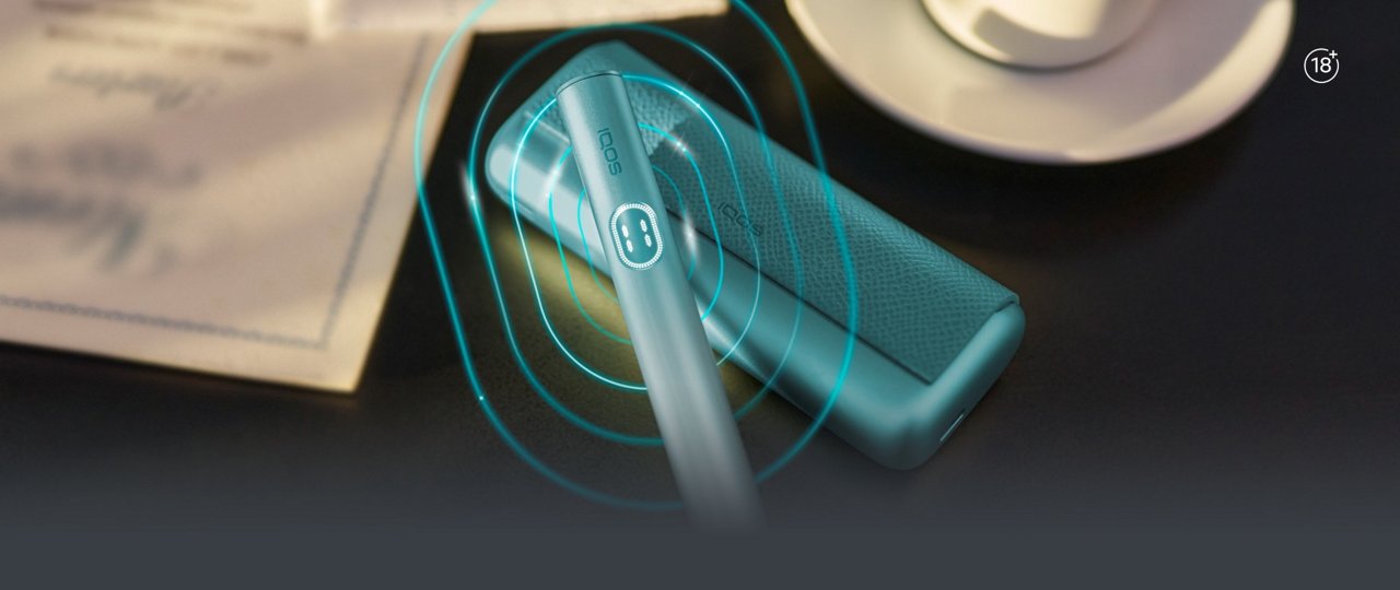 IQOS ILUMA i Prime device placed on a dark surface with a charging case nearby, surrounded by soft turquoise glowing ripple effects.