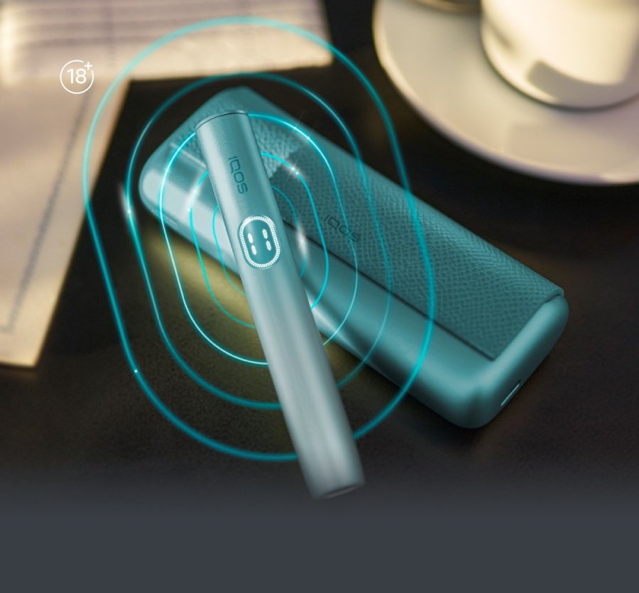 IQOS ILUMA i Prime device placed on a dark surface with a charging case nearby, surrounded by soft turquoise glowing ripple effects.