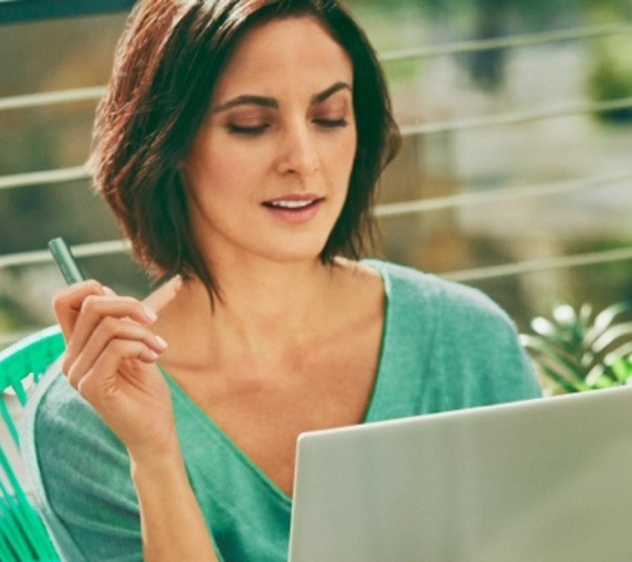 A woman holding an IQOS ILUMA device while looking at a laptop.