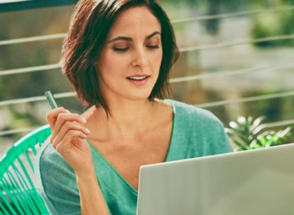 A woman holding an IQOS ILUMA device while looking at a laptop.