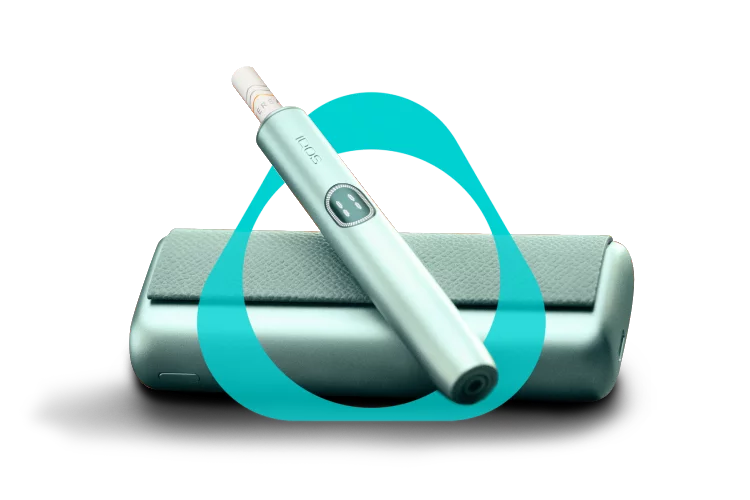 Close-up of an IQOS ILUMA i PRIME with a TEREA stick inserted on its holder. The holder is resting on top of its pocket charger, set against a warm orange-red gradient background.