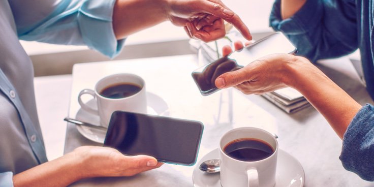 Two people holding phones over two cups of coffee.
