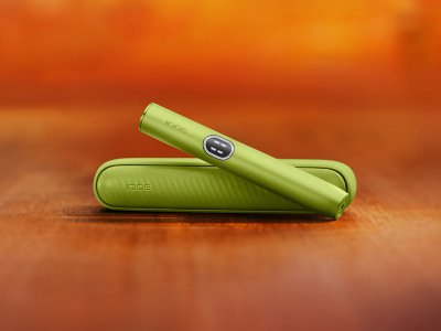 Appareil IQOS ILUMA i (stylet + chargeur de poche) couleur Vert Anis sur un fond dégradé orange