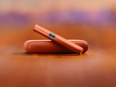 Zařízení IQOS ILUMA i v barvě Terracotta nad svou nabíječkou, s červeným pozadím