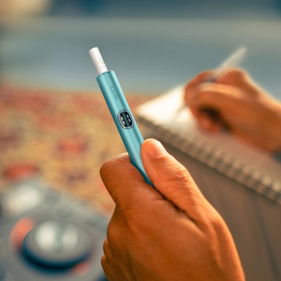 Hand holding a blue IQOS ILUMA i device, while writing notes