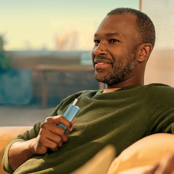 Person with green shirt holding IQOS Iluma I One device