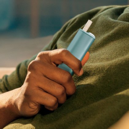 Hand holding a light blue IQOS ILUMA i ONE device