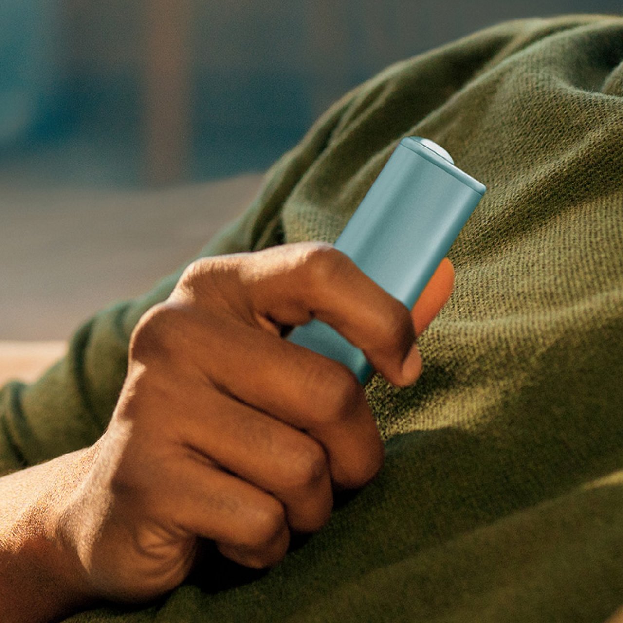 Рука держит светло-синее устройство IQOS ILUMA i ONE