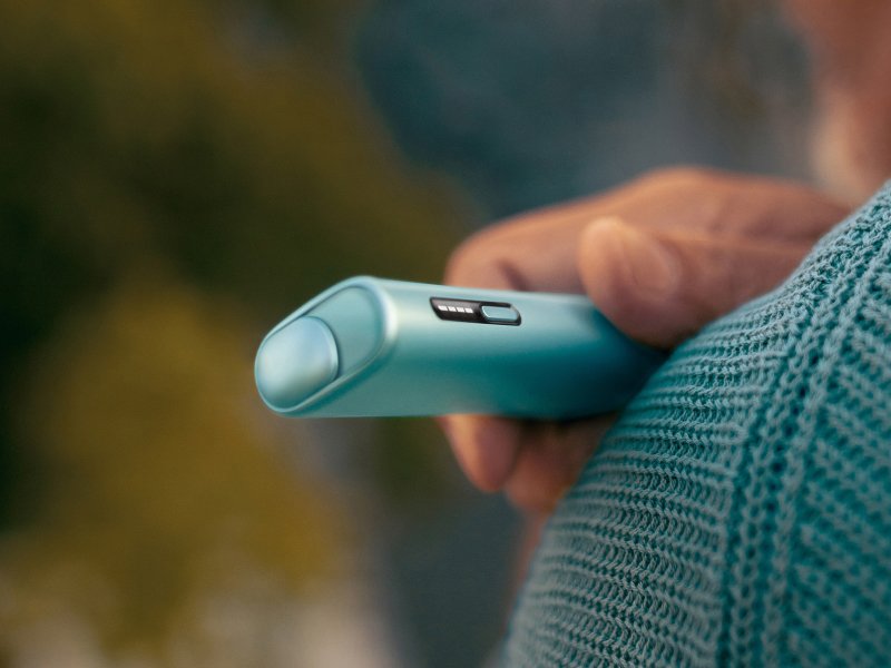 Person holding a Breeze Blue IQOS Iluma I One device  leaning on shoulder
