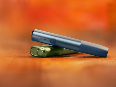 Modrý IQOS ILUMA i ONE nad zeleným IQOS ILUMA i ONE, s červeným pozadím