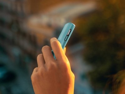 Hand holding a IQOS Iluma I One device on a dark background