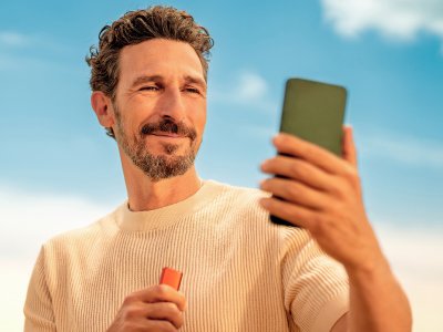 Muž hledící do svého telefonu a držící zařízení IQOS ILUMA i ONE