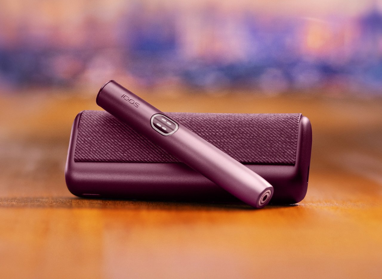Устройство IQOS ILUMA i PRIME гранатово-красного цвета над зарядным устройством