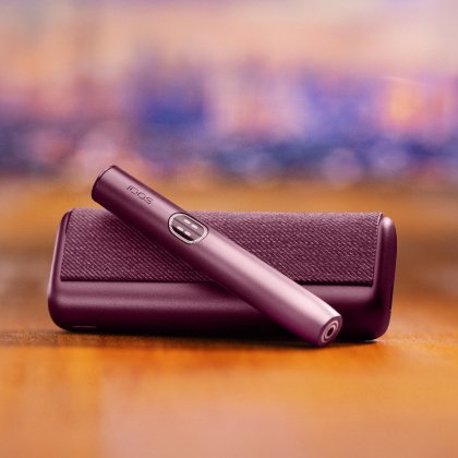Устройство IQOS ILUMA i PRIME гранатово-красного цвета над зарядным устройством