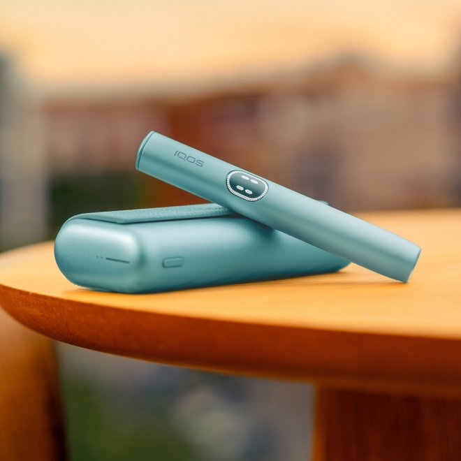 Držalo za IQOS ILUMA i PRIME v svetlomodri barvi Breeze Blue na žepnem polnilniku, na mizi.