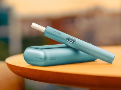 جهاز IQOS ILUMA i PRIME باللون الأزرق فوق الشاحن الخاص به، على الطاولة
