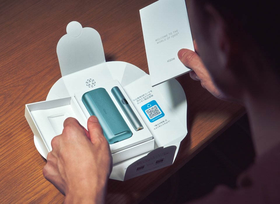 Detail of hands unboxing a blue IQOS ILUMA i PRIME device