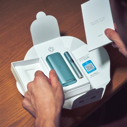 Detail of hands unboxing a blue IQOS ILUMA i PRIME device