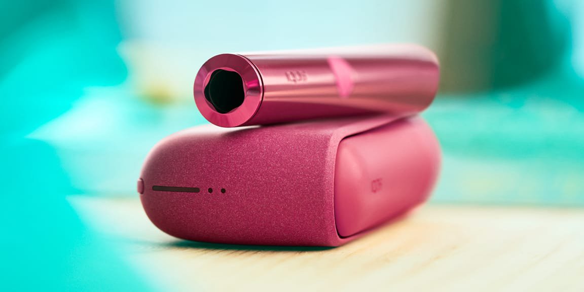 Ein sonnenuntergang-rotes IQOS ILUMA Gerät liegt auf einem Tisch