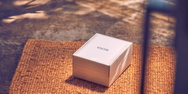An unopened IQOS device box on a rug.
