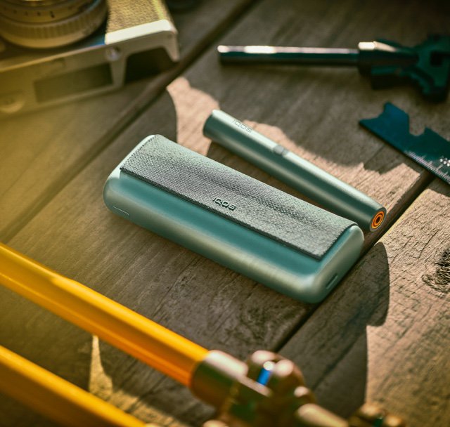 A Jade Green IQOS ILUMA PRIME Holder and Pocket Charger on a wooden table.