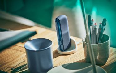 An IQOS ILUMA Pocket Charger in a charging dock with an IQOS Tray nearby.