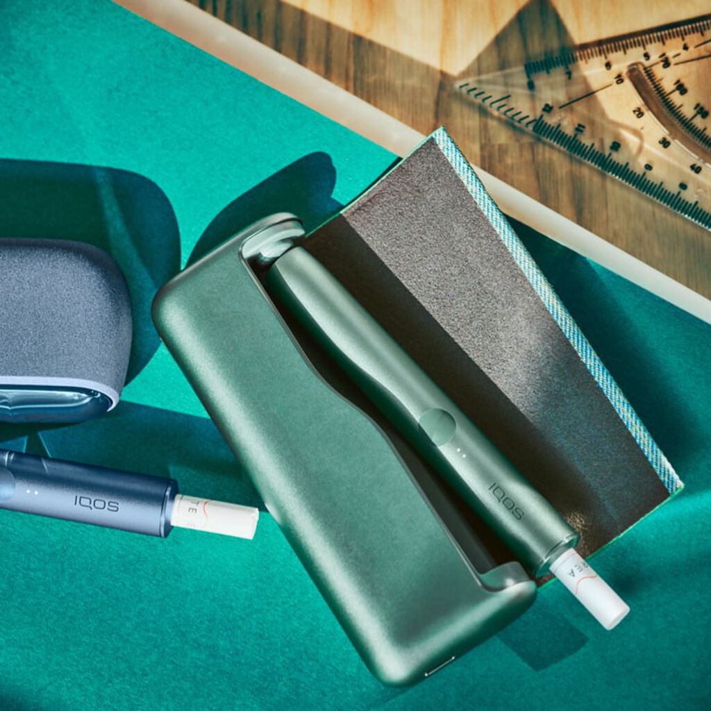 Jade green IQOS ILUMA device and charger on a desk.