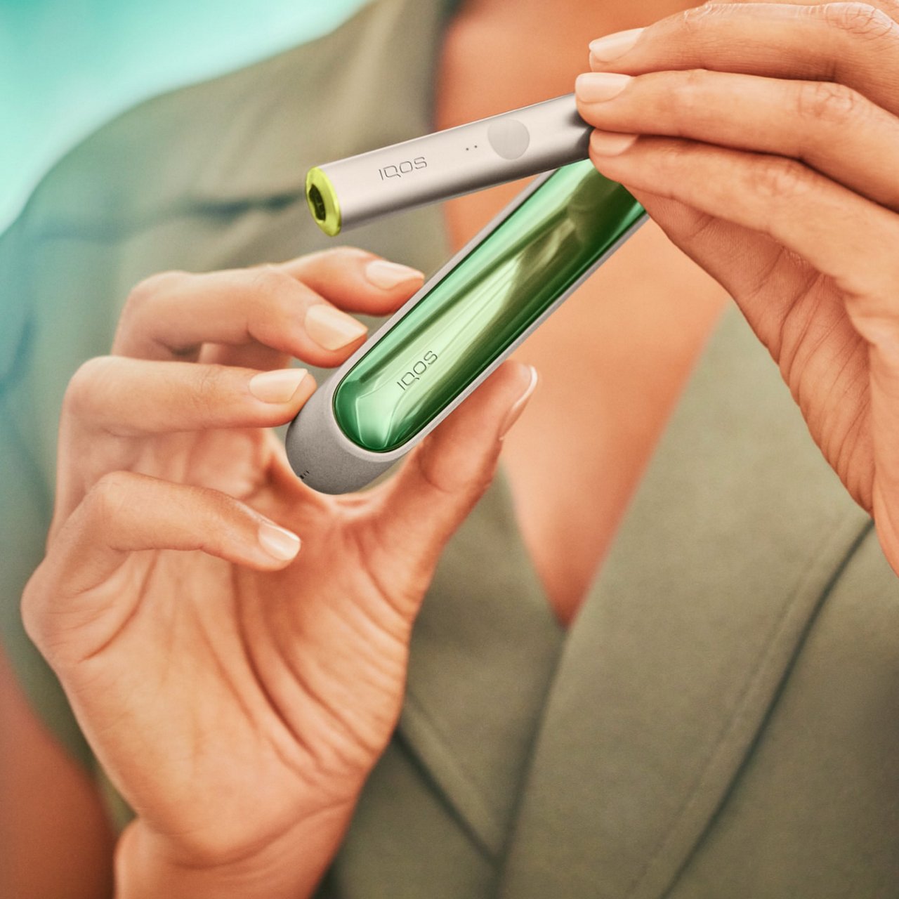 Manos sosteniendo un holder y cargador de IQOS ILUMA con carcasa lateral verde