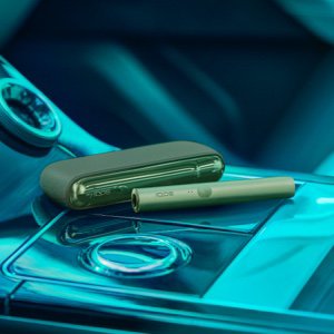 A Moss Green IQOS device sitting on a car console.