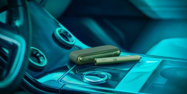 A Moss Green IQOS device sitting on a car console.