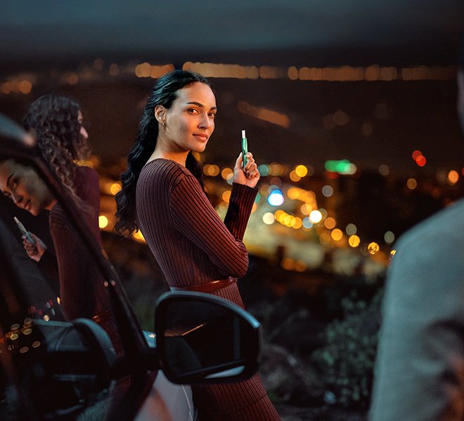 Woman with an IQOS ILUMA Jade Green holder and TEREA Stick leaning into a car.
