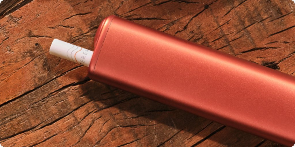 Red IQOS ILUMA i ONE device on wooden table