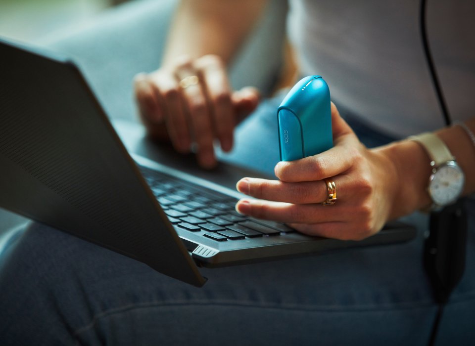 Woman holding IQOS ORIGINALS DUO Pocket Charger using a laptop 