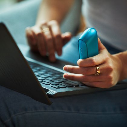  Woman holding IQOS ORIGINALS DUO Pocket Charger using a laptop