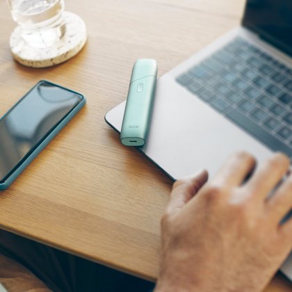  Man holding IQOS ILUMA ONE device using a laptop 